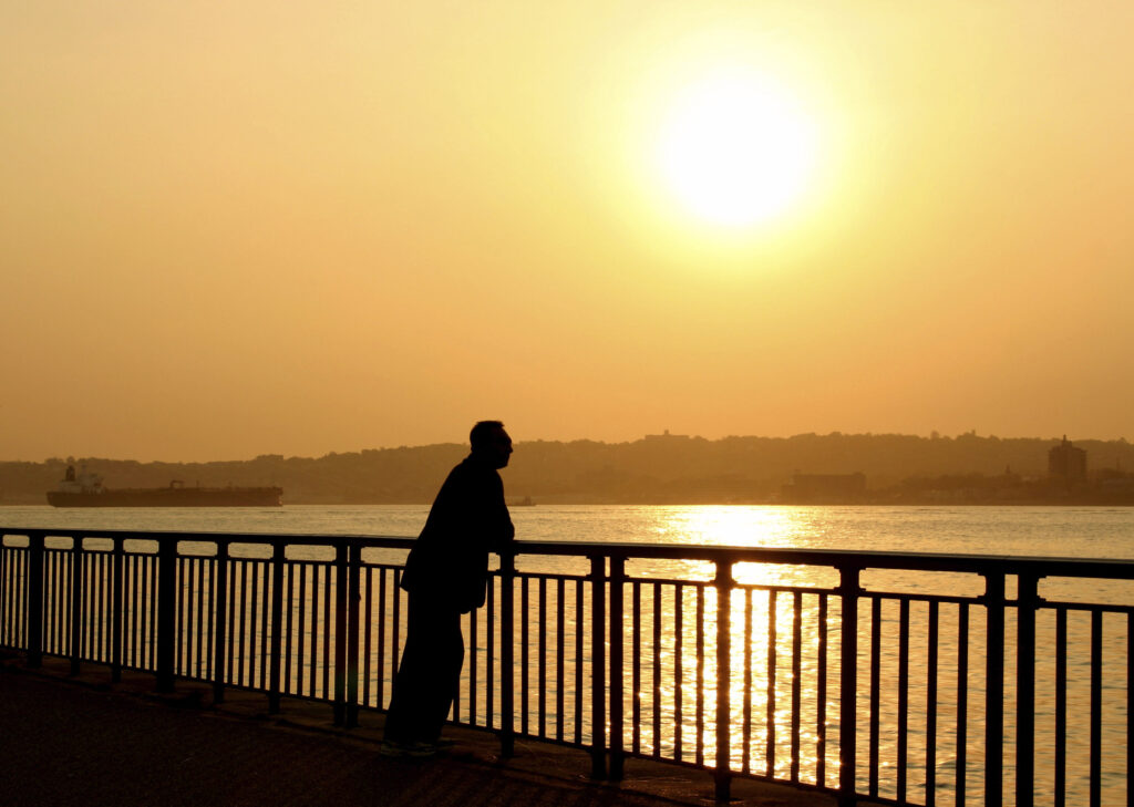 Persona reflexiva en penumbra junto a un lago al atardecer, evocando alta sensibilidad